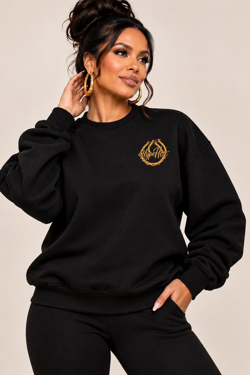 Model wearing a black HypeHer® sweatshirt with a gold Hoops emblem and gold bamboo hoop earrings.